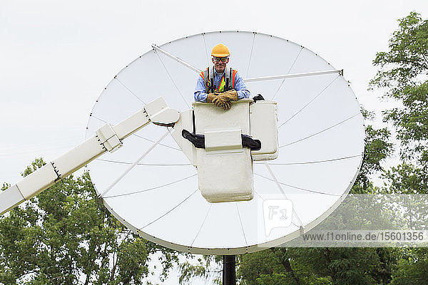 Communications engineer in bucket on truck in front of satellite dish