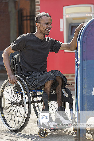 Mann im Rollstuhl  der an Spinaler Meningitis erkrankt ist  benutzt den öffentlichen Briefkasten