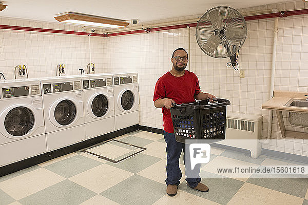 Afroamerikanischer Mann mit Down-Syndrom hält Wäschekorb in Waschküche