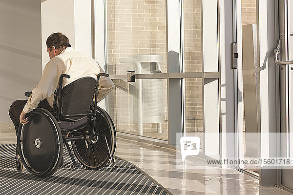 Geschäftsmann mit Querschnittslähmung im Rollstuhl im Eingang eines Bürogebäudes
