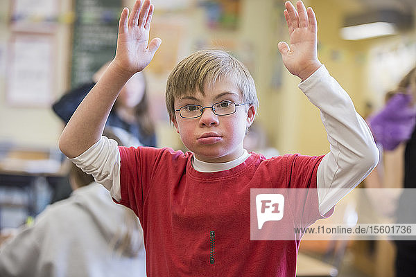 Junge mit Down-Syndrom mit erhobenen Armen in einem Klassenzimmer