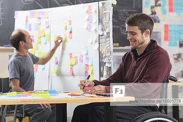 Studenten der Ingenieurswissenschaften schreiben Brainstorming-Ideen auf eine Projekttafel  ein Mann mit Rückenmarksverletzung und ein anderer mit Asperger