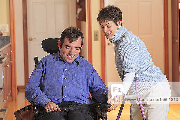 Frau mit Cerebralparese benutzt Krücken und hilft ihrem Mann mit Cerebralparese  seinen motorisierten Rollstuhl zu benutzen