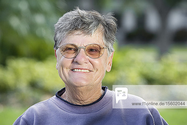 Ein älterer Mann sitzt lächelnd in einem Park.