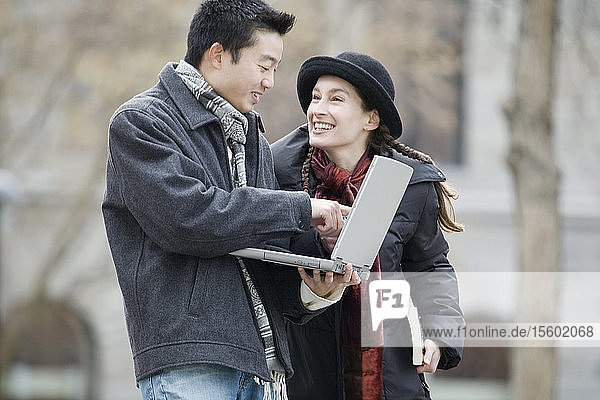 Seitenprofil eines jungen Mannes  der einen Laptop benutzt  und einer jungen Frau  die ihn ansieht