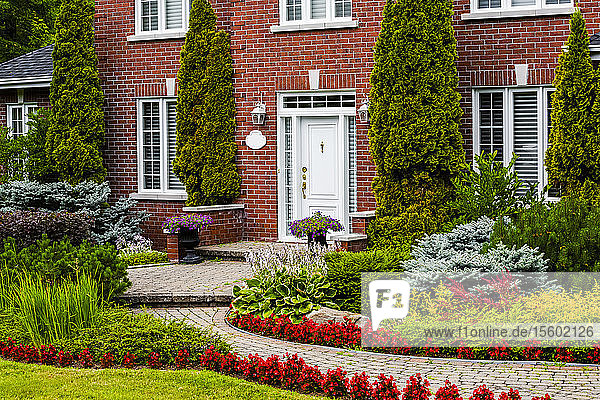 Stattliches Backsteinhaus mit einem gewundenen Weg und einer Gartenanlage mit Pflanzen und Blumen im Vorgarten; Hudson  Quebec  Kanada