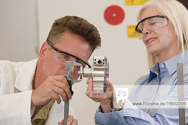 Engineering professors measuring a machine part with a vernier calliper