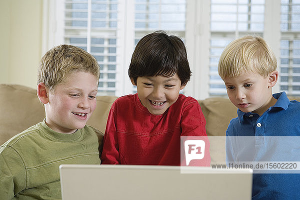 Vorderansicht von drei süßen Jungen  die auf einen Laptop schauen.