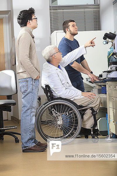 Professor mit Muskeldystrophie arbeitet mit Studenten der Ingenieurwissenschaften an einem Röntgenfluoreszenzanalysegerät in einem Labor