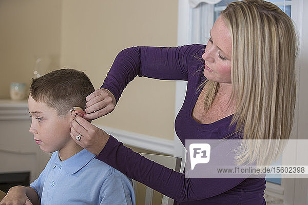Mutter  die ihrem hörgeschädigten Sohn zu Hause ein Hörgerät anlegt