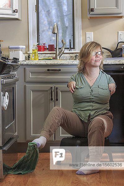 Frau mit TAR-Syndrom  die ein Küchenhandtuch mit den Füßen aufhebt