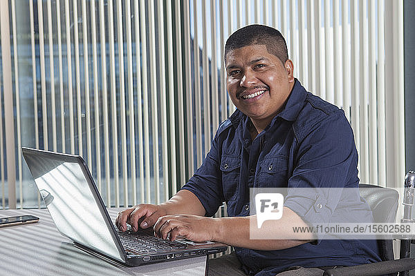 Hispanischer Mann mit Rückenmarksverletzung arbeitet in einem Büro