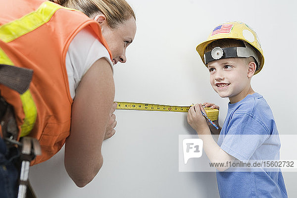 View of a woman and boy measuring wall with tape measure.