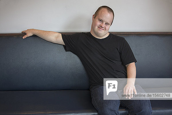 Porträt eines glücklichen Kellners mit Down-Syndrom auf dem Sofa in einem Restaurant