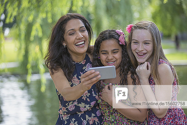 Happy Hispanic mother with two teen daughters with braces looking at text messages on mobile phone in park