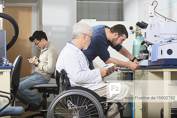 Ein Professor mit Muskeldystrophie und ein Ingenieurstudent benutzen das Handbuch zur Einstellung des Röntgenfluoreszenzanalysegeräts in einem Labor