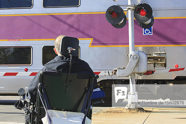 Mann mit Rückenmarksverletzung wartet mit seinem motorisierten Rollstuhl auf einen öffentlichen Zug