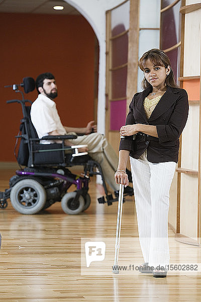 Porträt einer Frau mit einem auf einem Rollstuhl sitzenden Mann im Hintergrund.