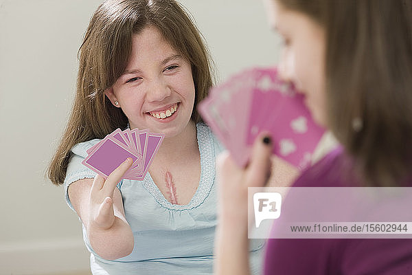 Zwei Teenager-Mädchen spielen Karten  Teenager-Mädchen mit Geburtsfehler im Gespräch mit einem Mobiltelefon