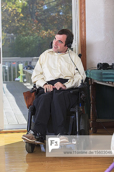 Mann mit zerebraler Lähmung im motorisierten Rollstuhl benutzt seine Kopfhörer