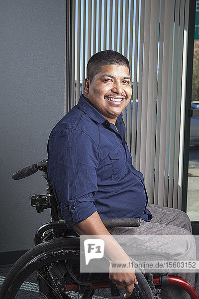 Hispanischer Mann mit Rückenmarksverletzung im Rollstuhl in einem Büro