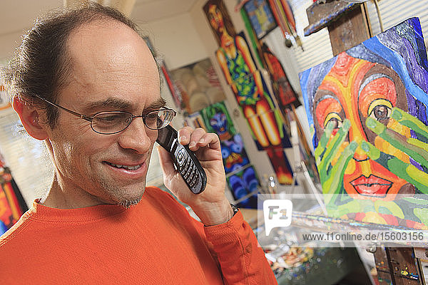 Mann mit Asperger-Syndrom in seinem Malatelier mit seinem Mobiltelefon