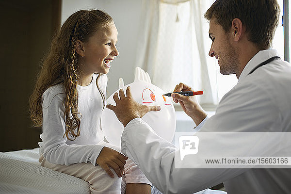 Young doctor drawing a face onto a balloon for a young patient