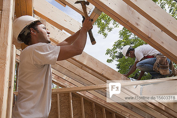 Zimmerleute beim Einbau einer Dachluke auf dem Dach eines im Bau befindlichen Hauses