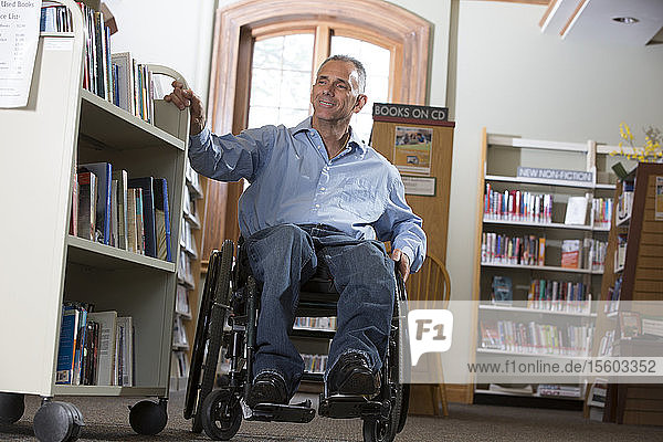 Man in a wheelchair with a Spinal Cord Injury moving a shelf of books in a library