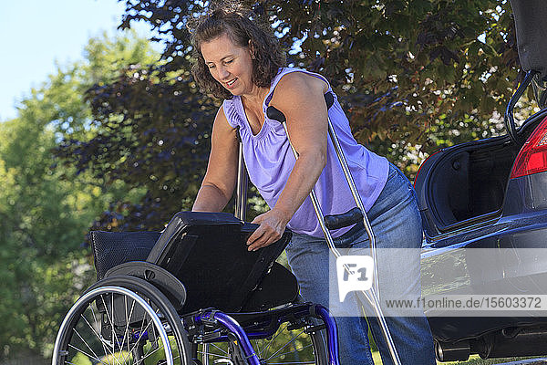 Frau mit Spina Bifida benutzt Krücken  um den Rollstuhl nach einer Reise im Auto zusammenzusetzen