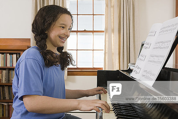 Hispanisches Mädchen  das ein Notenblatt liest und auf einem Klavier spielt