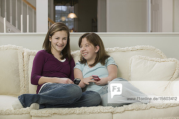 Two teenage girls sitting on a couch and using mobile phones  one with birth defect
