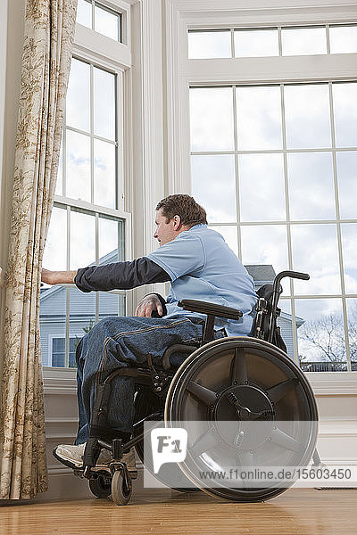 Ein querschnittsgelähmter Mann im Rollstuhl schaut aus dem Fenster seiner barrierefreien Wohnung