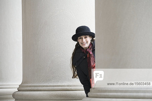Portrait of a young woman peeking from behind a column and smiling