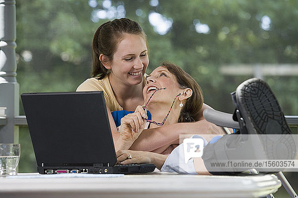 Young woman hugging her disabled mother from behind and smiling