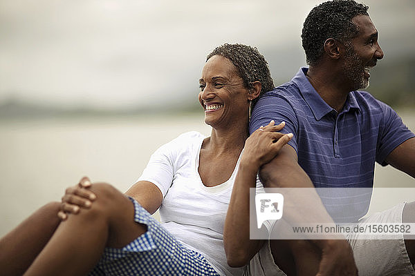 Glückliches Paar im mittleren Erwachsenenalter  das zusammen am Rande einer Uferpromenade sitzt