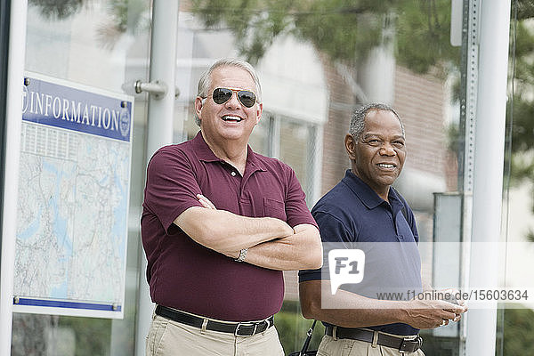 Two businessmen standing at a bus stop and smiling