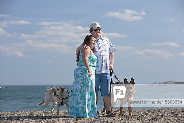 Young couple with visual impairments and service dogs on the beach