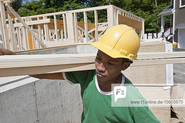 Zimmermann trägt eine Planke auf einer Baustelle