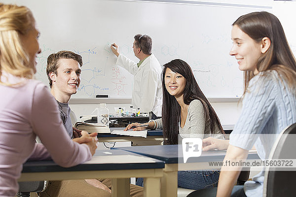 Students talking in an engineering class while the professor is writing on the white board