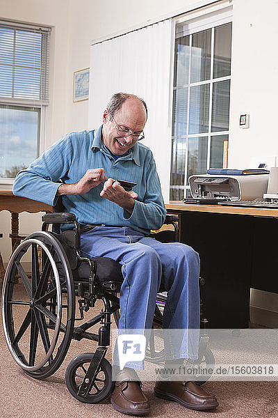 Man with Friedreich's Ataxia in wheelchair using a smartphone with deformed hands