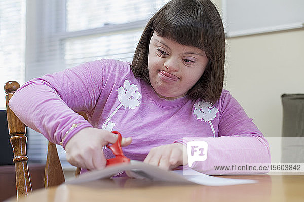 Girl with Down Syndrome cutting a paper with scissors