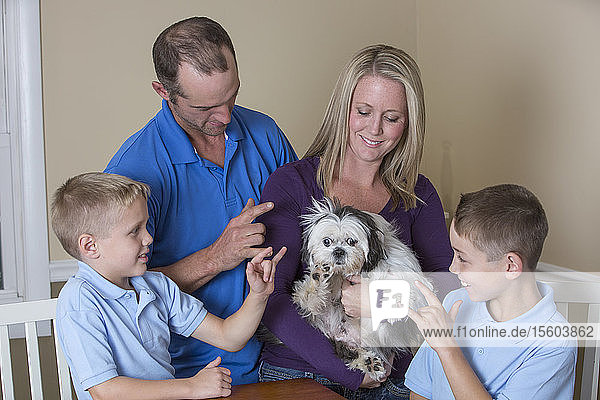 Um einen Tisch sitzende Familie mit Hörbehinderung  die Love and New Puppy in amerikanischer Zeichensprache beschreibt