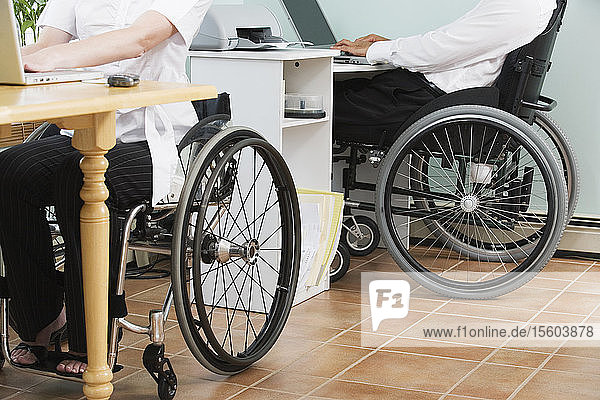 Man with a woman sitting in wheelchairs with a Spinal Cord Injury and using laptops