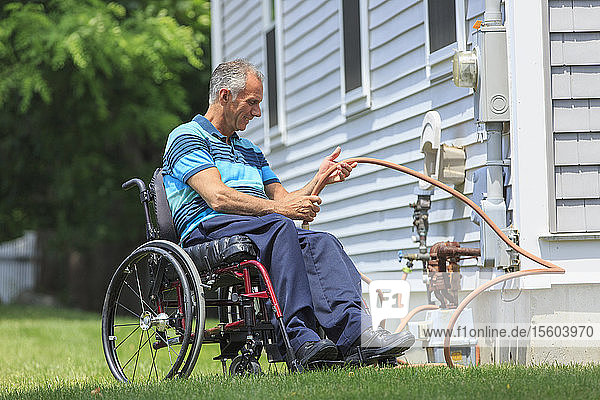 Mann mit Rückenmarksverletzung im Rollstuhl beim Verlegen des Schlauchs auf dem Hinterhof seines Hauses