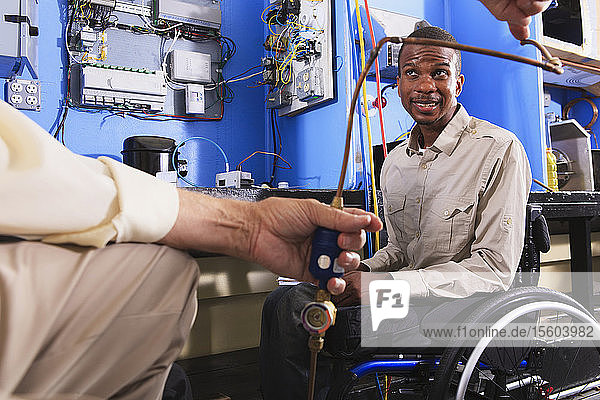 Ausbilder demonstriert einem Schüler im Rollstuhl die Hochdruckleitung einer Klimaanlage im HVAC-Klassenzimmer