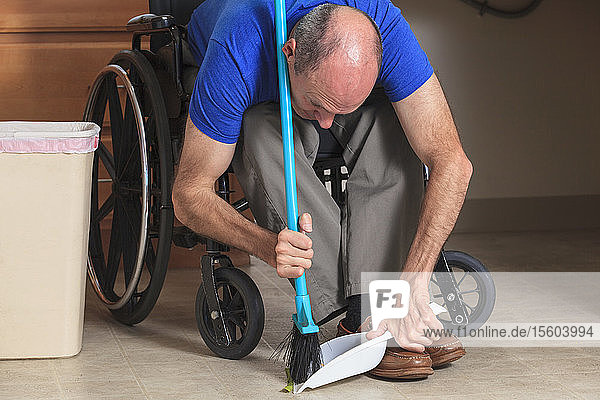 Mann mit Friedreich-Ataxie und deformierten Händen reinigt sein Haus vom Rollstuhl aus mit einem Besen