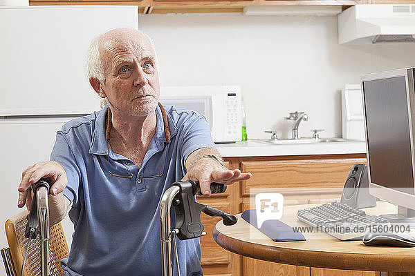 Mann mit Ataxie hält seine Gehhilfe mit seinem Computer in der Küche