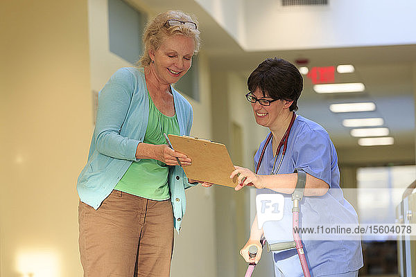 Krankenschwester mit Cerebralparese an Stöcken schaut sich Patientenakten an