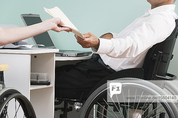 Mittlere Schnittansicht eines erwachsenen Mannes  der mit einer Rückenmarksverletzung im Rollstuhl sitzt und seine Hausaufgaben macht